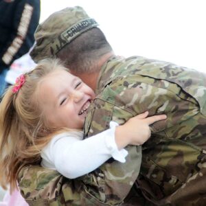 A soldier in uniform hugs a little girl with blonde hair